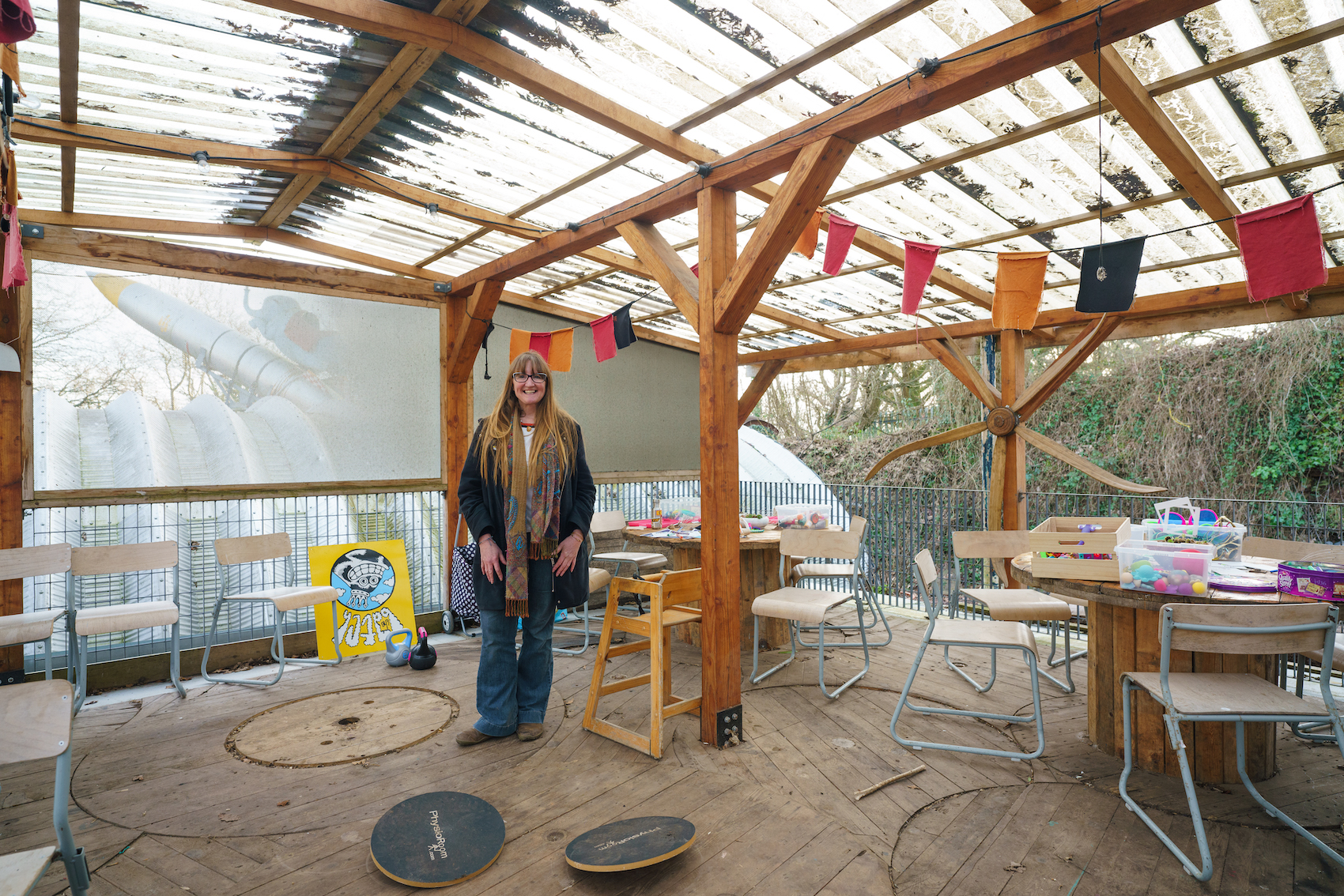 A woman stands in a DIY work space surrounded by chairs.