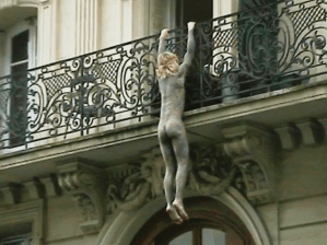 A naked man hangs from a balcony